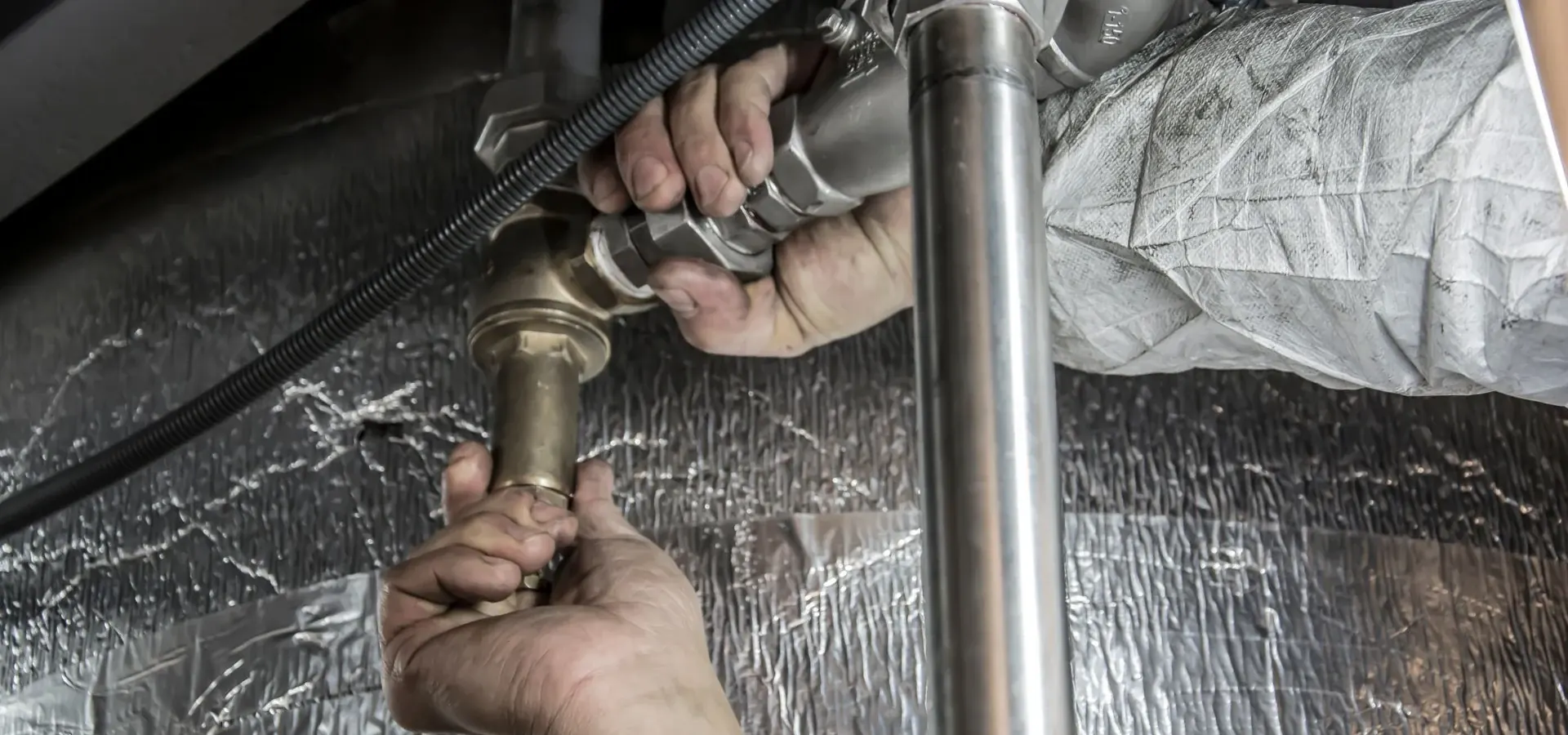 Plumber tightening a brass fitting on an insulated pipe run
